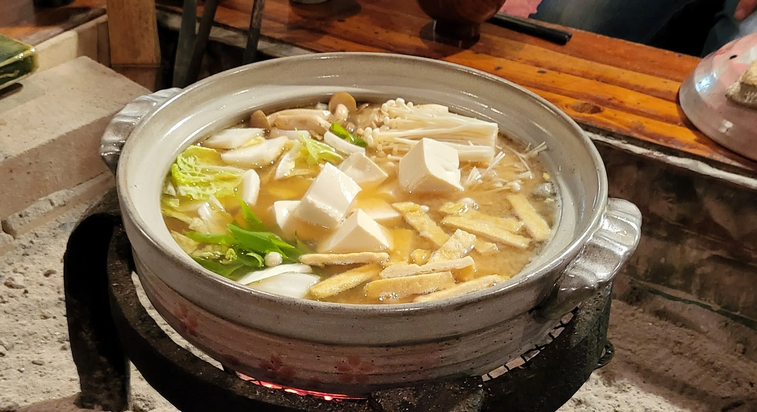A bubbling nabe hot pot of tofu and vegetables cooking over charcoal at a rural Japanese inn
